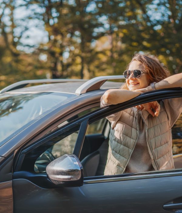 Happy woman driver traveling by car in forest enjoying freedom and nature